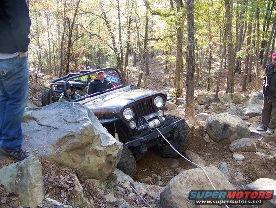 Brown Jeep Wrangler navigating rocky terrain with a winch line attached