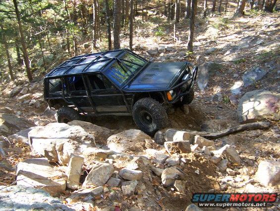 Modified off-road SUV with a roll cage navigating a rocky trail