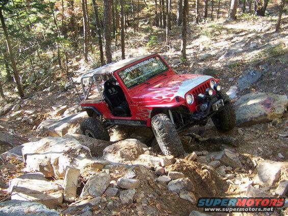 Red Jeep Wrangler with flame decals navigating a rocky trail