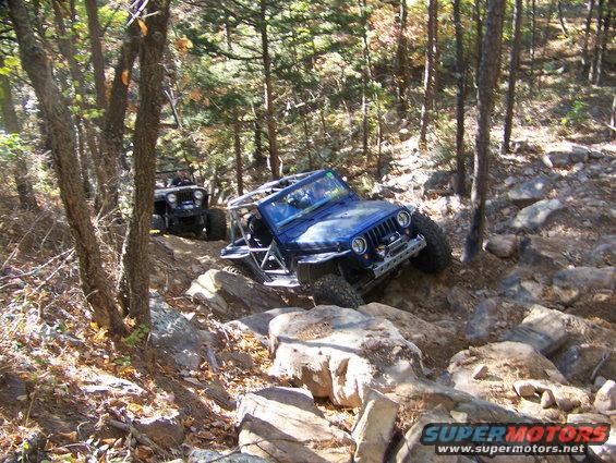 Blue Jeep Wrangler with roll cage navigating rocky terrain