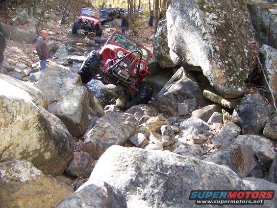 Red Jeep Wrangler navigating a rocky trail with other vehicles behind