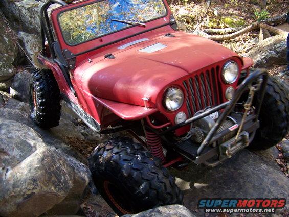 Red Jeep navigating rocky terrain, equipped with a winch