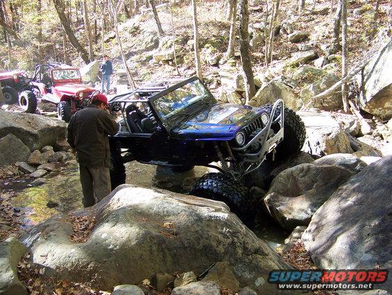 Two modified Jeeps off-roading over rocks and through water, with people observing