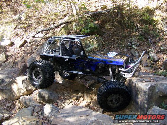 Modified Jeep on rocks, blue flames on hood, roll cage, large tires