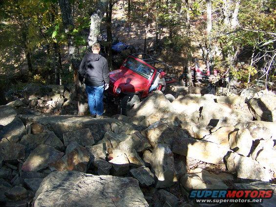 Red off-road vehicle stuck on rocks with a person standing nearby