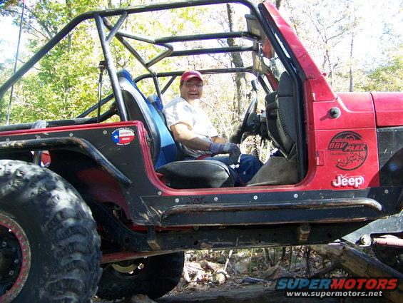 Red Jeep Wrangler with roll cage, off-road tires, and a man driving