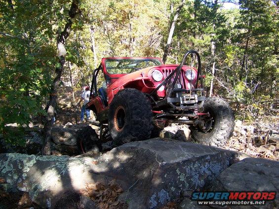 Red Jeep with large tires navigating rocky terrain
