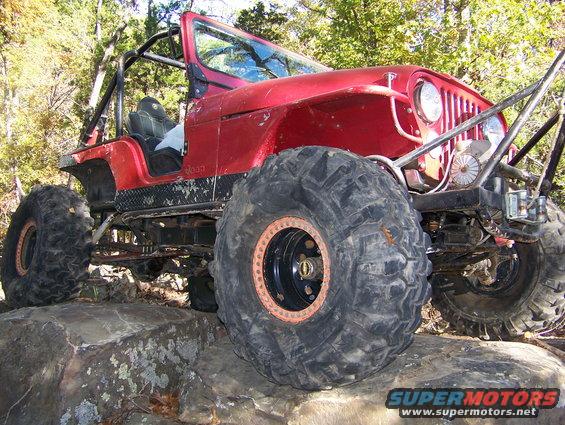 Red Jeep Wrangler with oversized tires on rocks