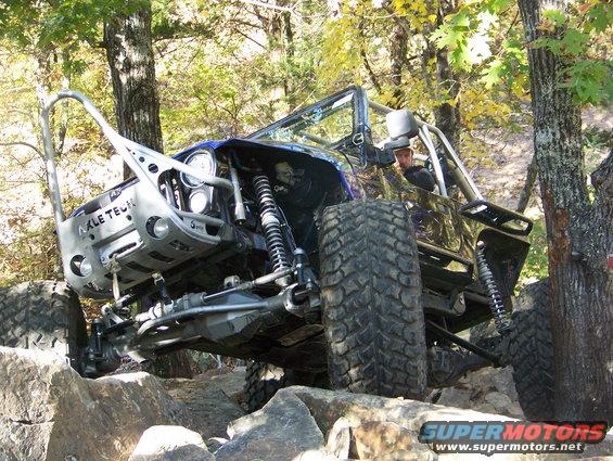 Off-road Jeep climbing over rocks with a person wearing a hat inside