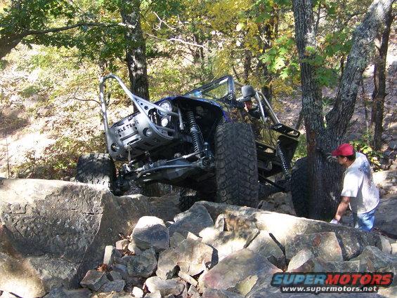 Modified off-road vehicle with large tires navigating rocky terrain