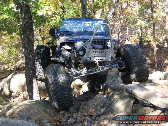 Blue Jeep Wrangler with large tires and roll cage navigating rocky terrain