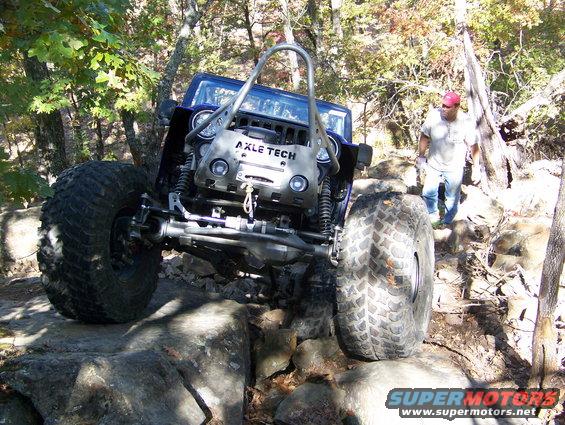 Off-road Jeep with large tires navigating rocky terrain. 'AXLE TECH' visible on front