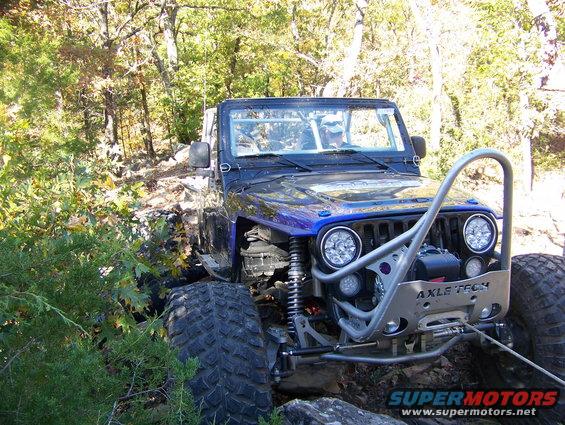 Modified Jeep Wrangler with large tires and custom bumper on a rocky trail