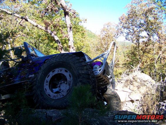 Blue Jeep with roll cage and large tires climbing over rocks on a trail
