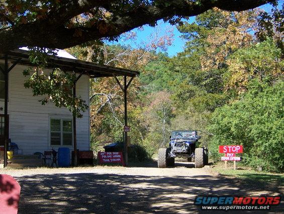 modified Jeep Wrangler with large tires on a dirt road near a building and trees