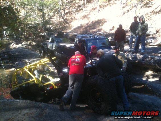 Off-road vehicles stuck on rocks, people assisting