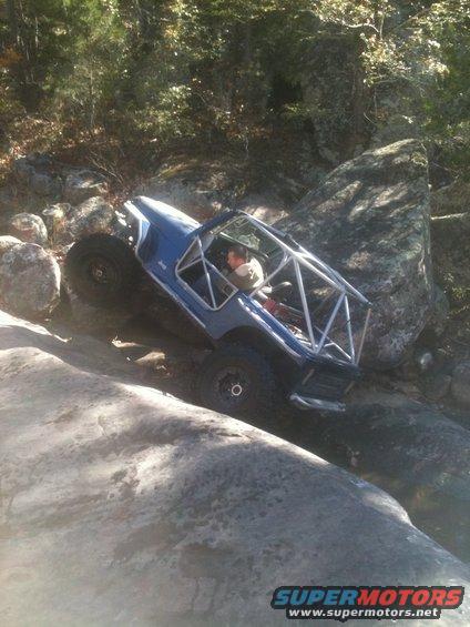 Blue off-road vehicle with roll cage climbing over rocks