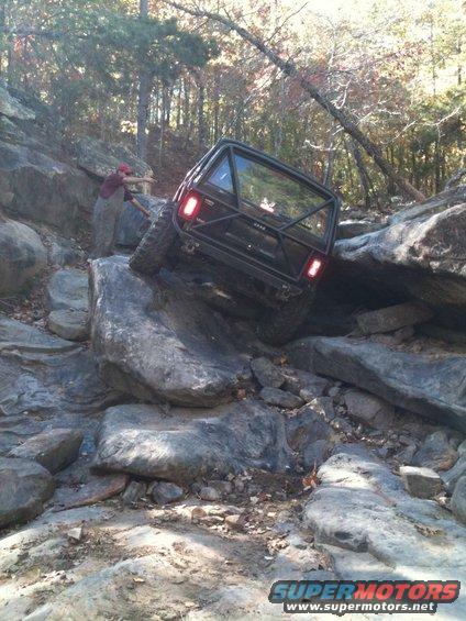 Modified off-road vehicle with roll cage climbing over large rocks on a trail