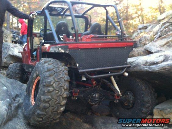 Modified Jeep Wrangler with roll cage and large tires on rocks. Another vehicle is visible behind it