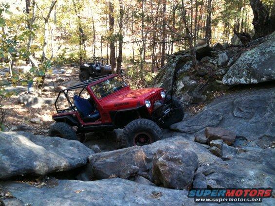 Red Jeep Wrangler navigating rocky terrain with another off-road vehicle in the background