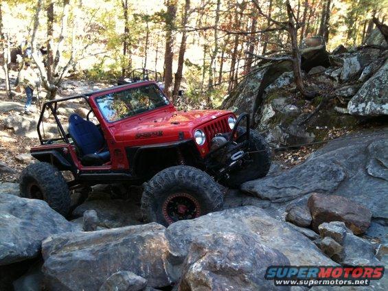 Red Jeep Wrangler with a roll cage and winch navigating rocky terrain