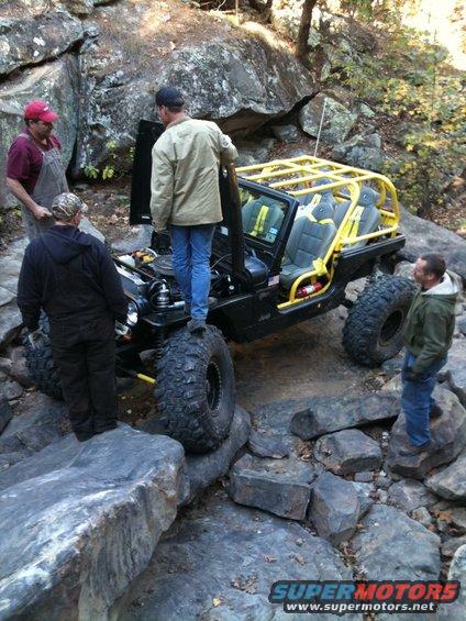 Black Jeep Wrangler with yellow roll cage navigating rocky terrain