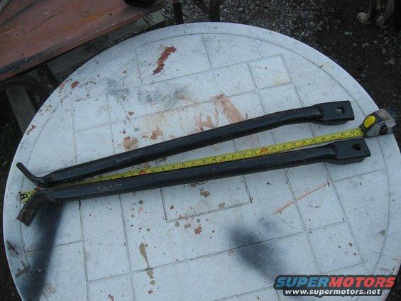 Two black metal bars laid on a white table with a yellow measuring tape next to them