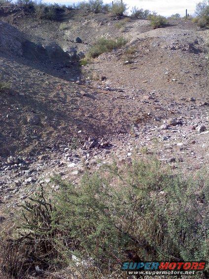 Desert landscape with scrub brush and rocks. Watermark reads www.supermotors.net