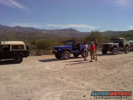 Several Ford Broncos parked on a dirt road in a desert with mountains in the background