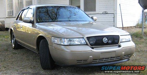 Gold Mercury Grand Marquis parked outside a house. Front grille and headlights are visible
