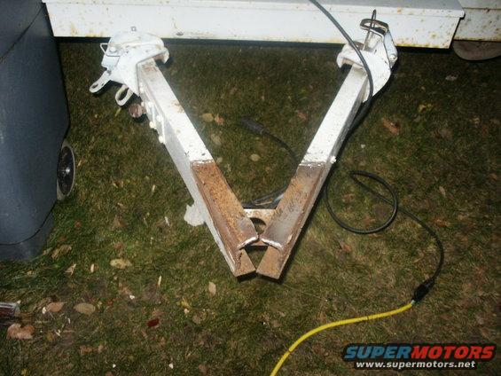 Trailer hitch assembly with white painted metal and rust, connected to a dark gray object with a wheel