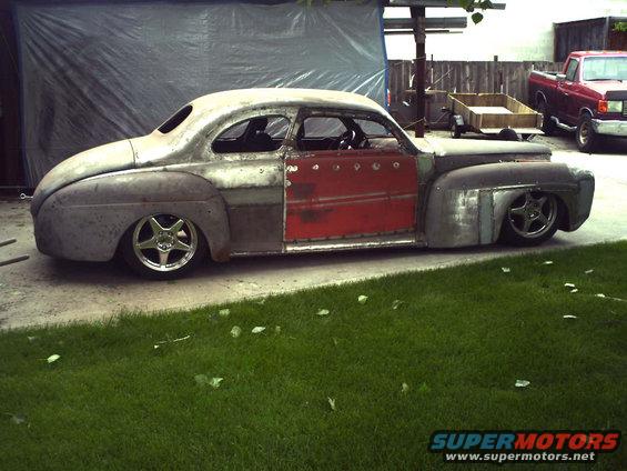 Unfinished coupe hot rod, bare metal body with red doors, lowered suspension, custom wheels, parked on concrete