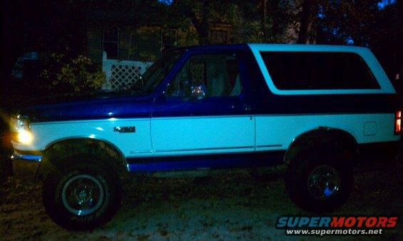 Blue and white Ford Bronco, side view, lifted suspension, aftermarket wheels, dark exterior