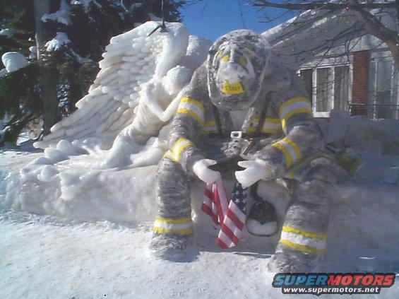 Ice sculpture of a firefighter holding American flags, with an angel behind, covered in snow and ice