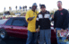 1992 Ford Mustang - Three men pose with a trophy next to a red coupe at a drag racing event.