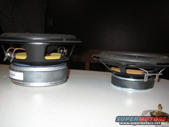 Two car speakers on a white surface. One has a white label on its side