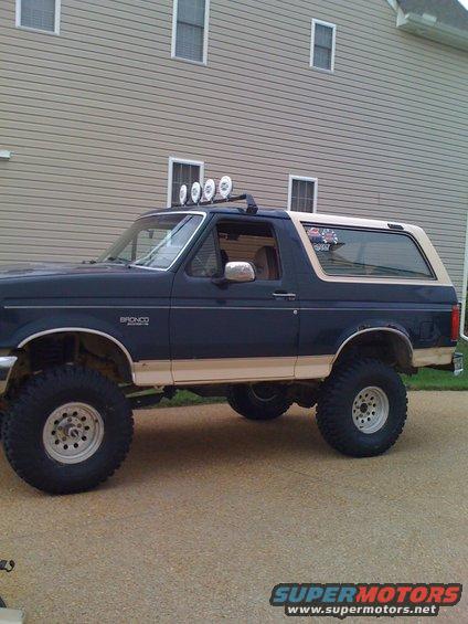 Dark blue and tan Ford Bronco with off-road tires and roof lights, seen from the side