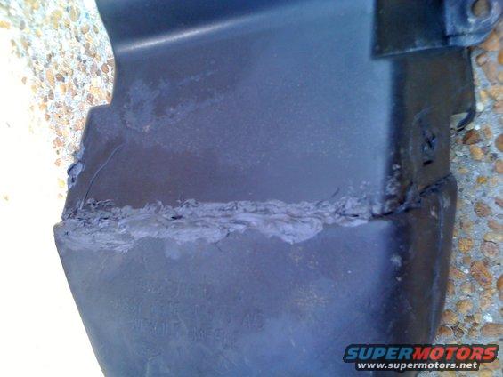 Close-up of a cracked and repaired black plastic car trim piece with visible text underneath