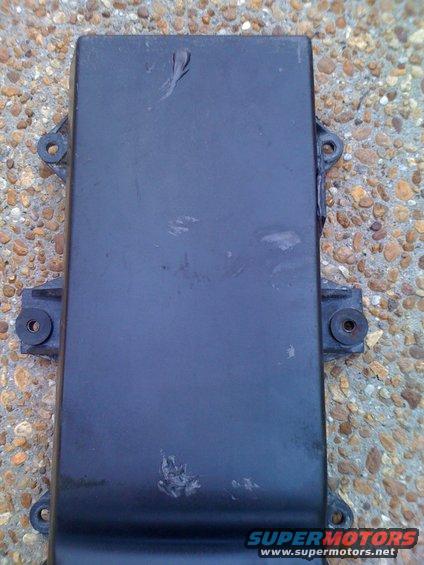 Black rectangular automotive part with two mounting brackets on the left and one on the right, resting on a gravel surface