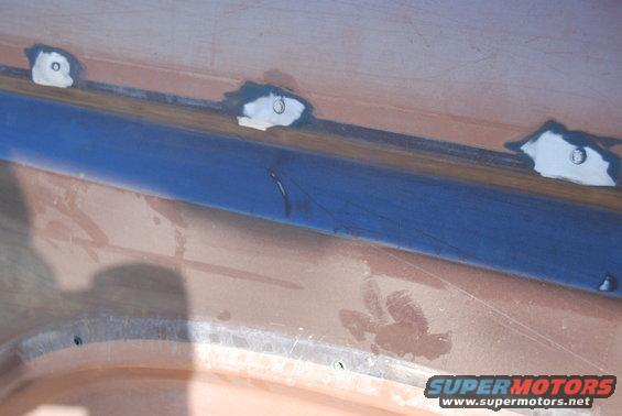 Car body panel with blue tape and white primer spots, showing signs of repair
