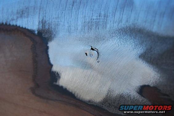 Metal body panel with primer and filler, showing a small dent being repaired