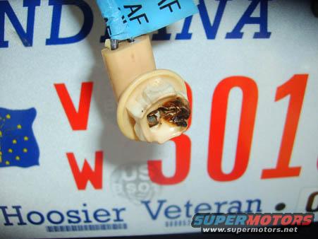 Burnt electrical connector with blue tape, in front of Indiana license plate 'V W 301'
