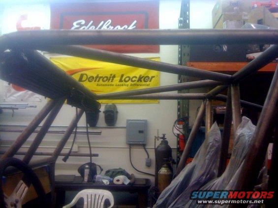 Roll cage structure inside a vehicle, with a Detroit Locker banner and Edelbrock sign in the background