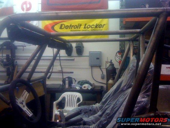 Custom roll cage structure in a workshop with a Detroit Locker banner in the background
