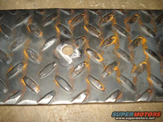 Diamond plate metal with rust and a drilled hole. Supermotors.net logo at bottom right