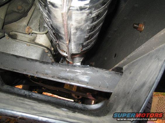 Underside view of a chrome exhaust pipe and black chassis components, with a Supermotors.net watermark
