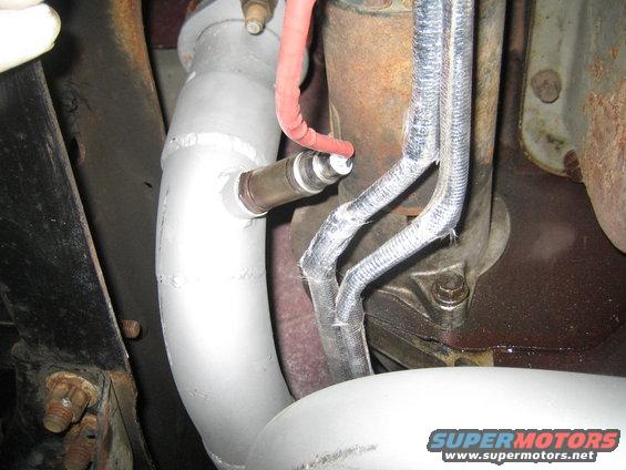 Close-up of an exhaust pipe with an oxygen sensor attached, near engine components