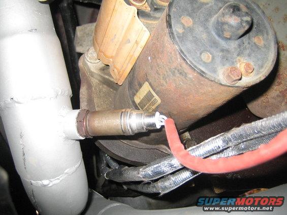 Exhaust pipe with oxygen sensor attached to a rusty metal component with a label