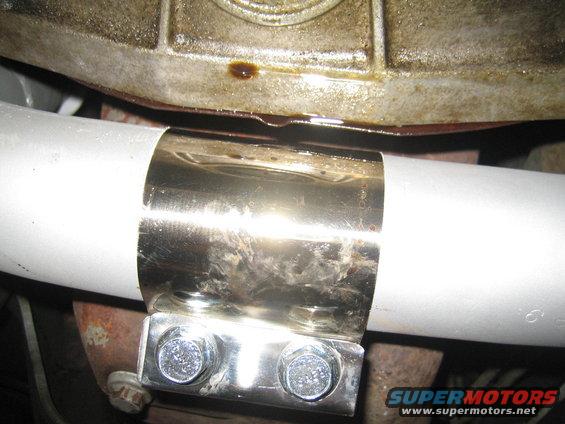 Exhaust pipe with a shiny metal clamp and two bolts. Oil is visible on the metal casing above