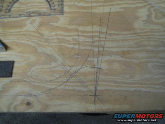 Plywood surface with pencil lines forming a diagram, a protractor ruler, and a metal block